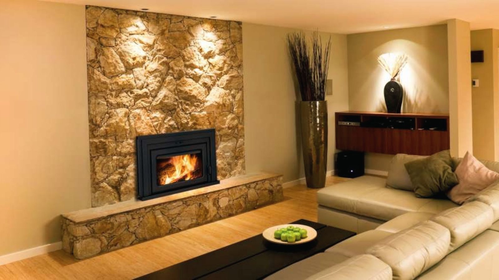 Basement stone fireplace insert with raised hearth, tall vase decor and cream sectional sofa.