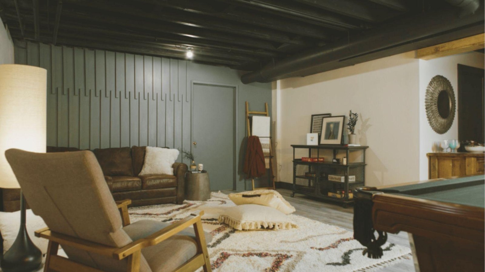 Cozy basement lounge with a black-painted open joist ceiling and exposed ductwork above a leather sofa and pool table.