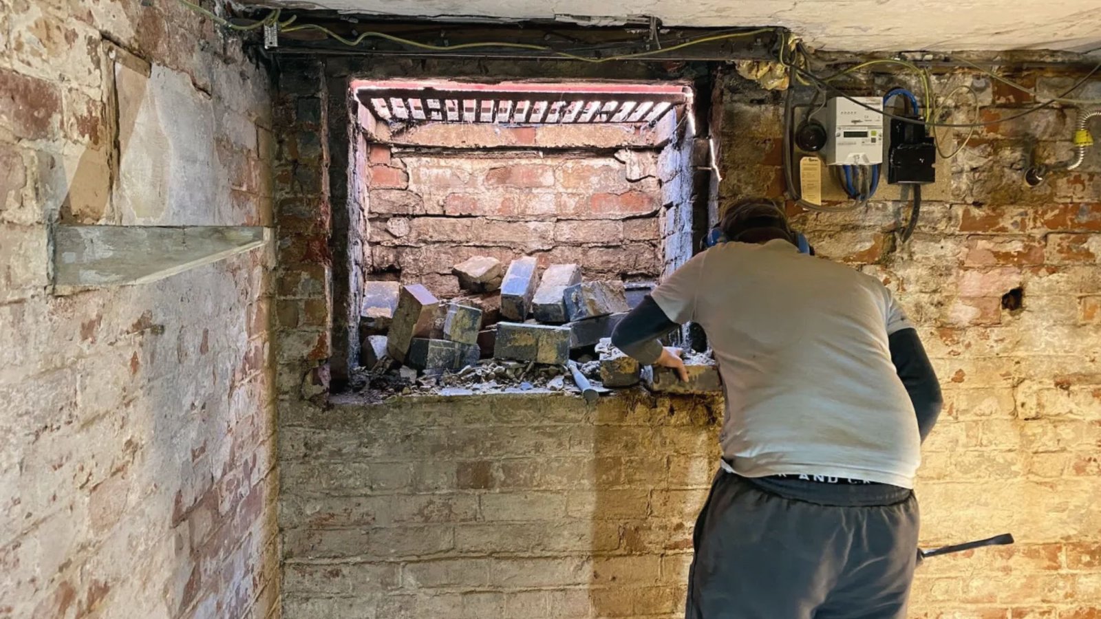 Worker removes old bricks from basement window openings during renovation to install new frames.