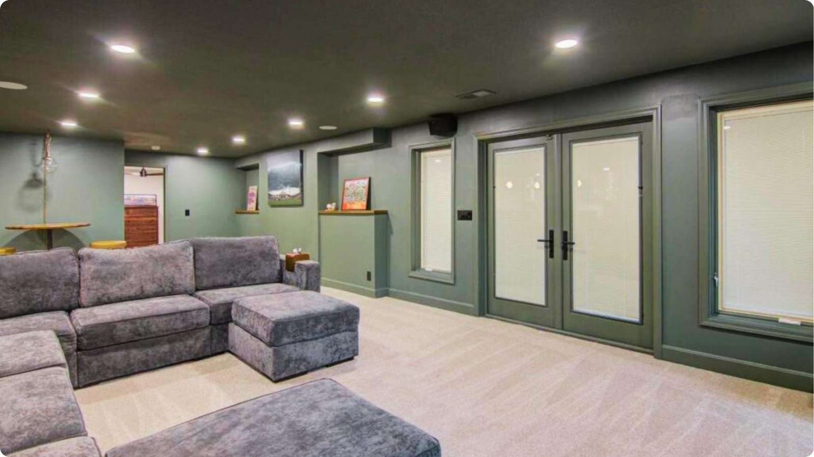 Finished low-ceiling basement lounge with sage green walls, recessed lighting, and large sectional sofa.