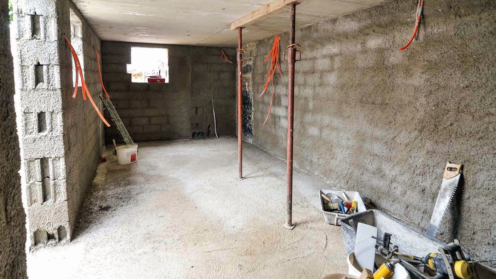 Unfinished basement with concrete block walls and tools, prepared for waterproofing installation work