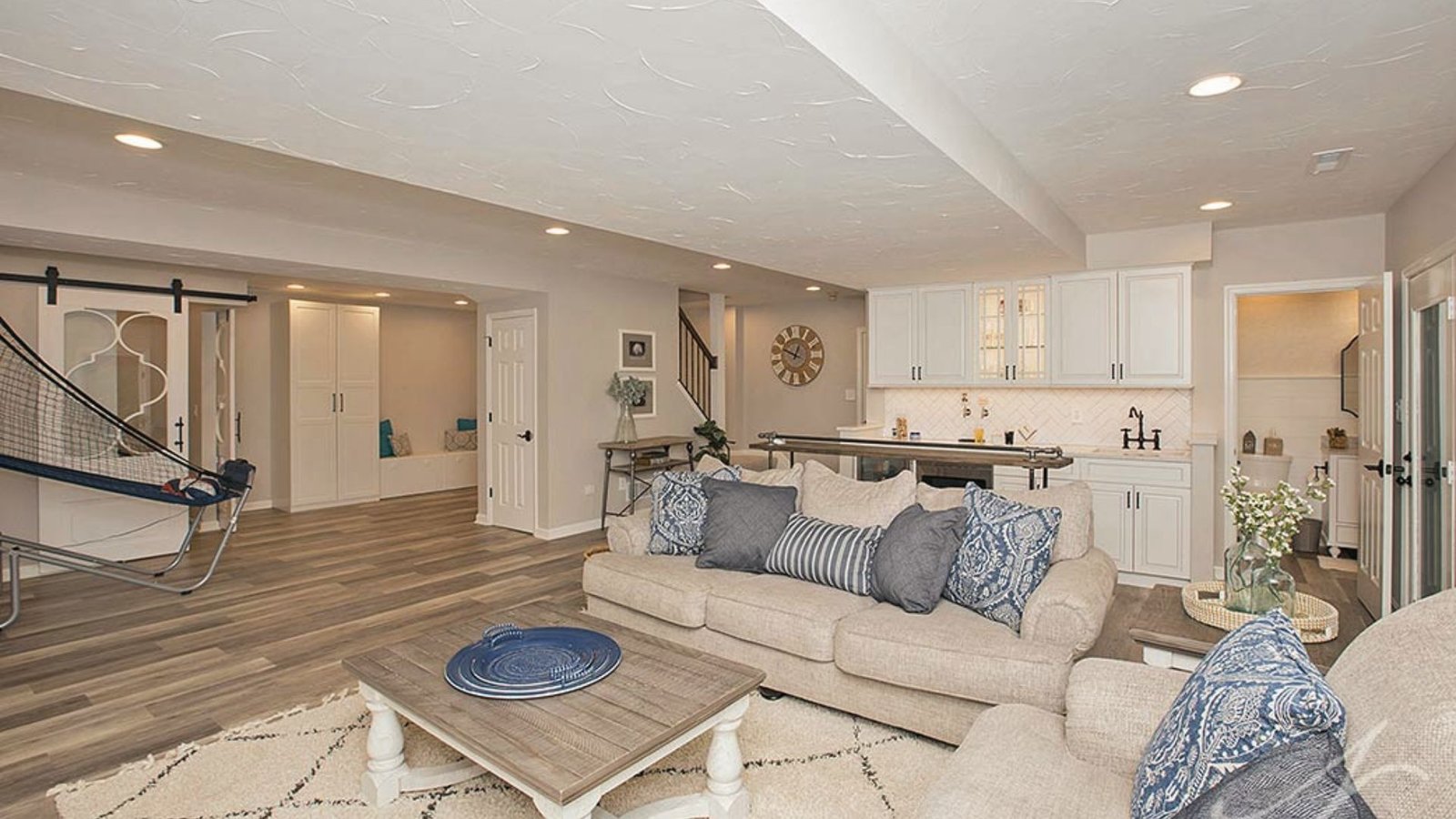 Open basement family room with kitchenette, sofa, wood floors, barn doors and basketball arcade game.