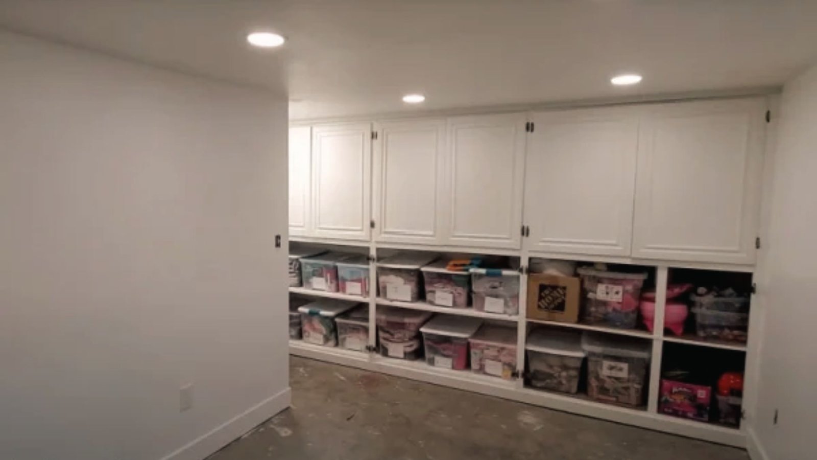 Organized basement storage room with white cabinets, labeled bins and shelving for household items.