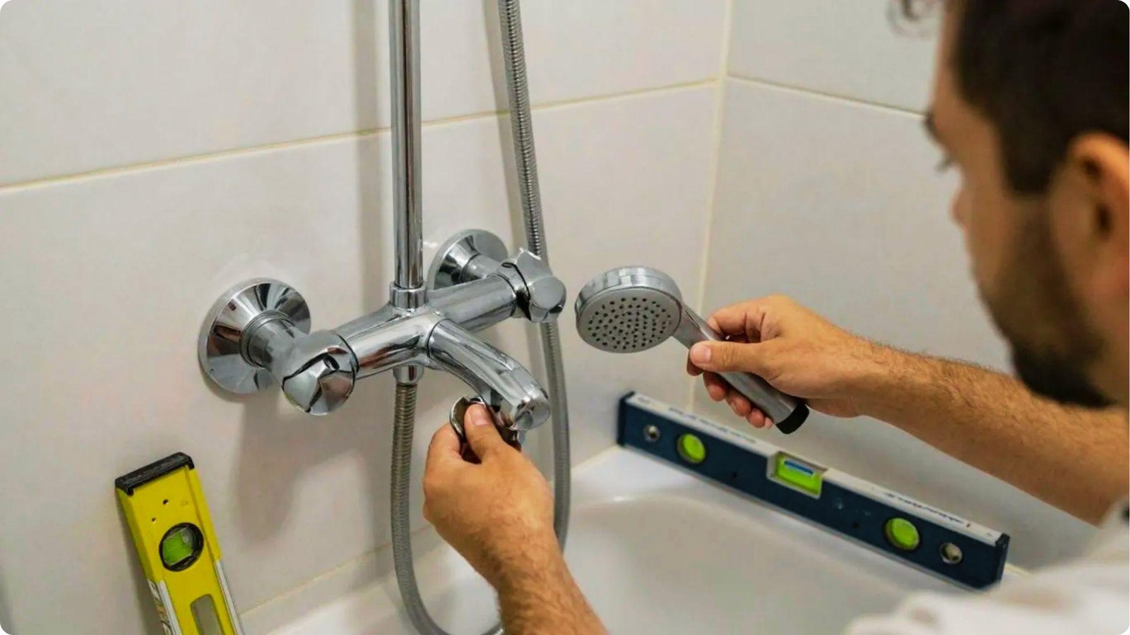 Person installing a handheld shower head with chrome fixtures, yellow and blue levels visible.