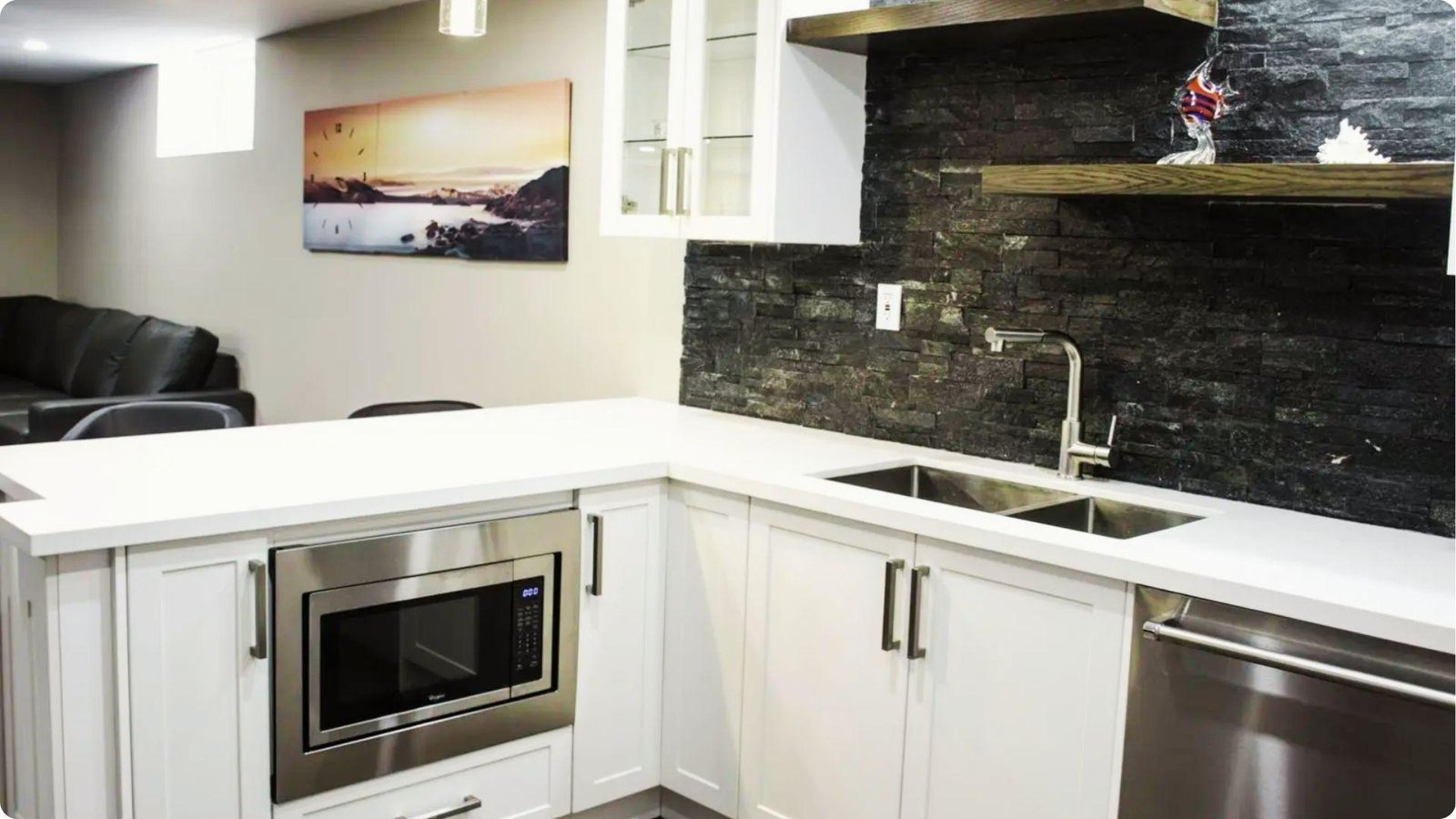 Modern basement kitchenette with white shaker cabinets, stacked stone backsplash, and stainless steel appliances.