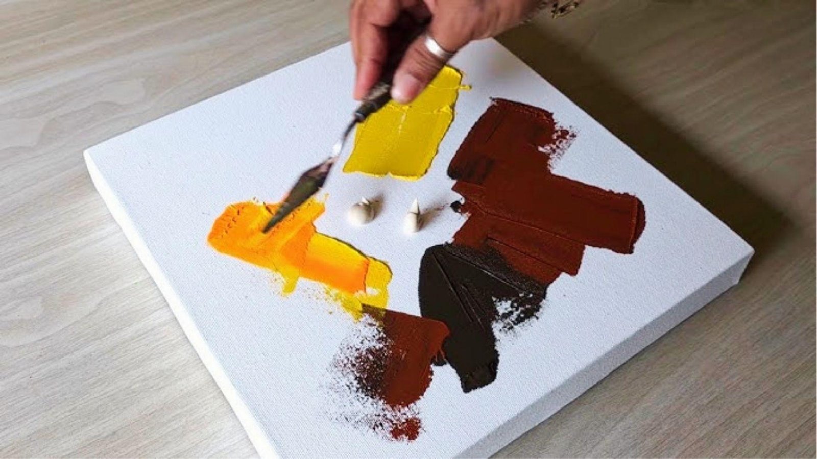 Hand mixing yellow and brown paint on canvas for DIY basement wall color selection during basement renovation cost planning.