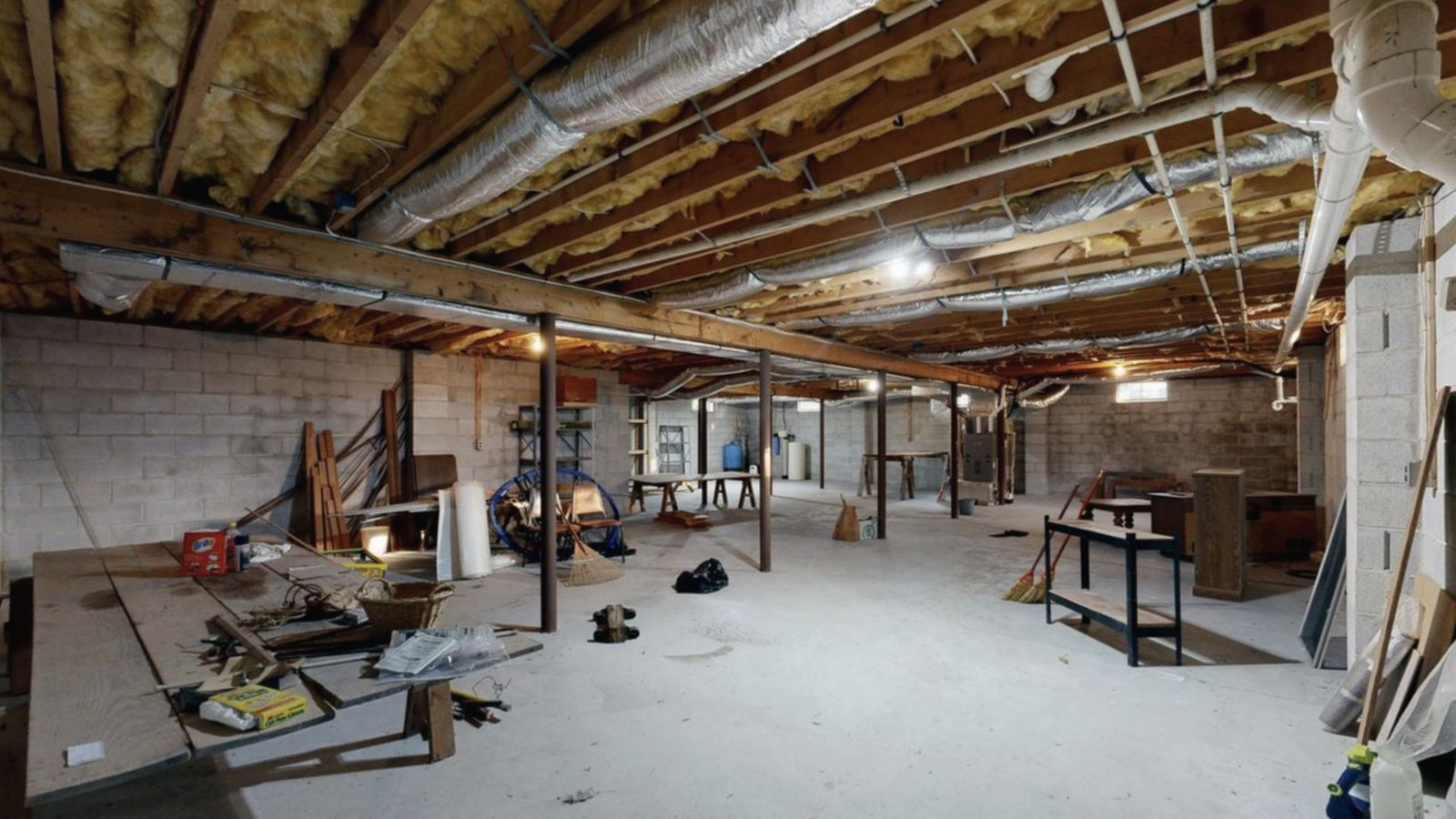 Unfinished basement layout with exposed joists, support posts, concrete floor and workshop tools.