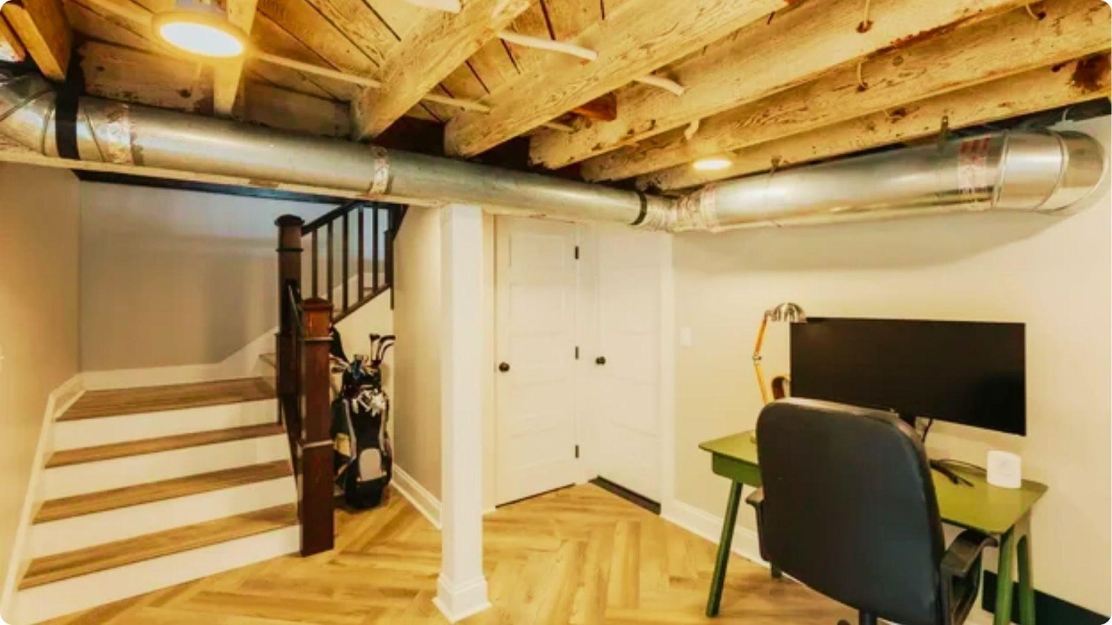 Basement home office with exposed wood joists, ductwork, and herringbone wood flooring.