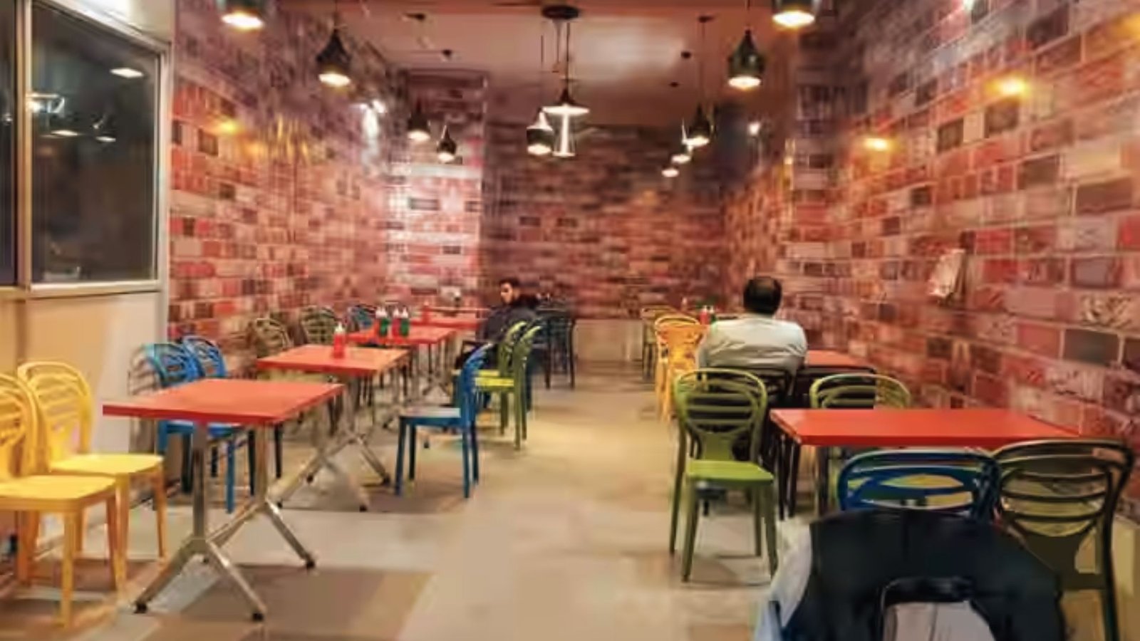 Industrial basement cafe style dining with brick walls, red tables and multicolor chairs for groups.