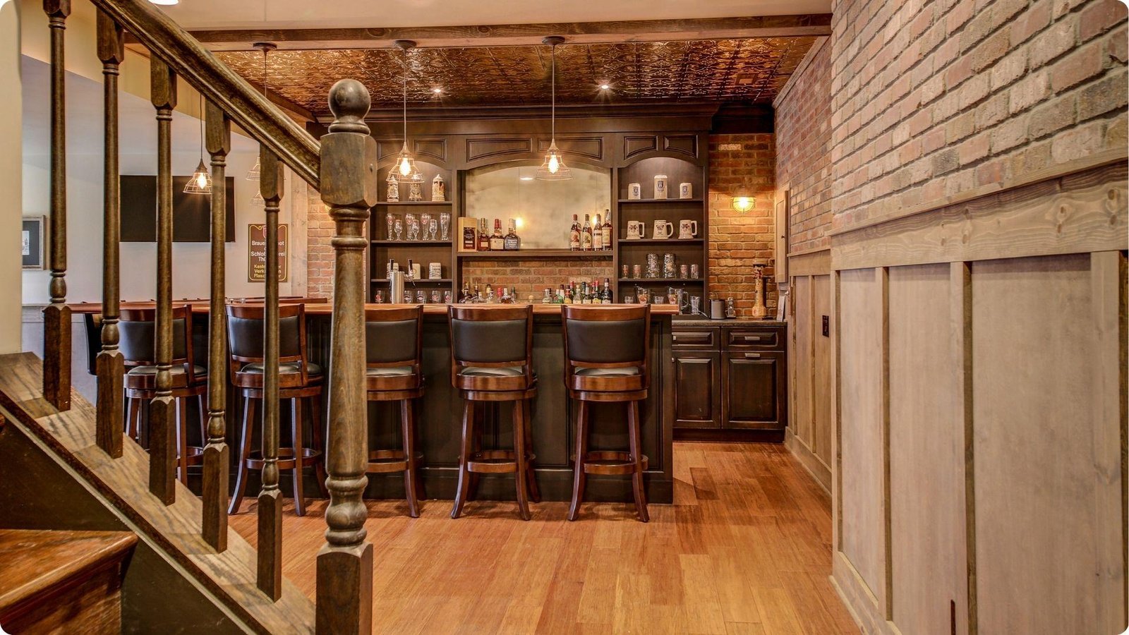 English basement bar area with exposed brick walls, dark wood cabinetry, and pendant lighting over bar stools.