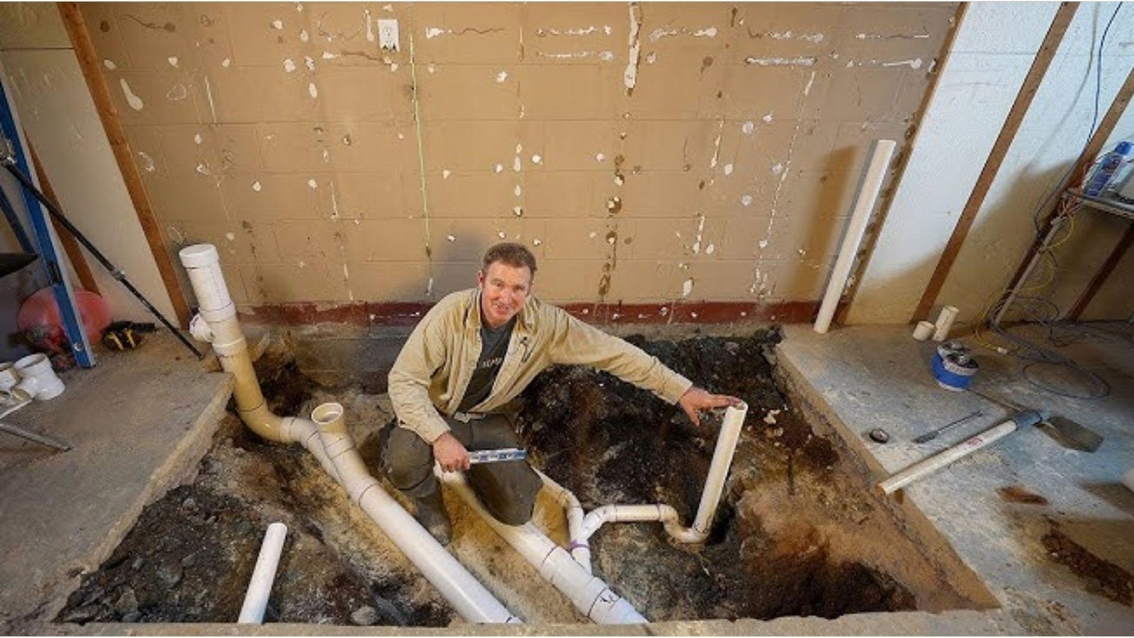 Plumber installing basement bathroom PVC drain pipes in excavated floor