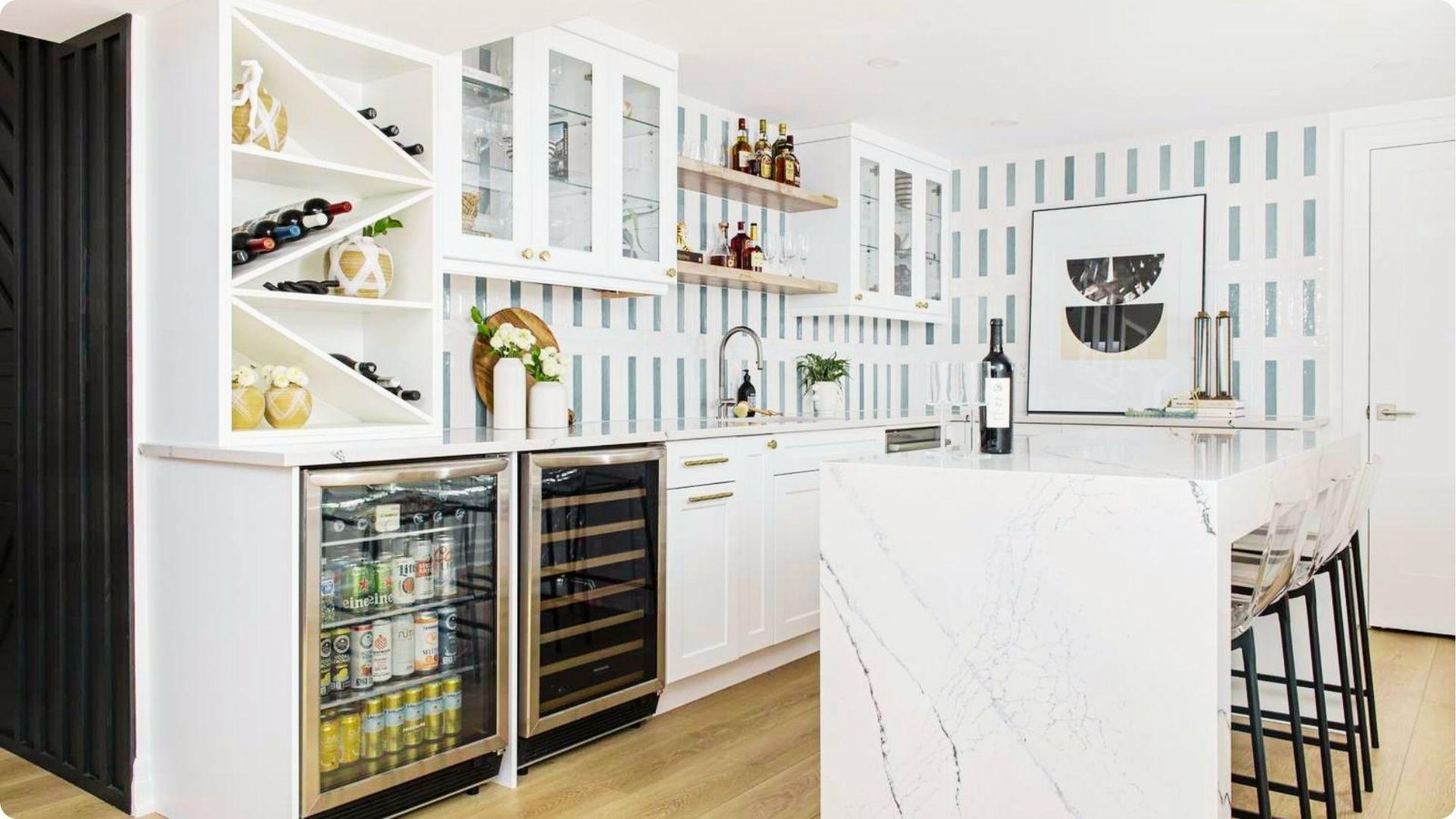 Bright basement wet bar with white cabinetry, blue-striped tile backsplash, and marble waterfall island.