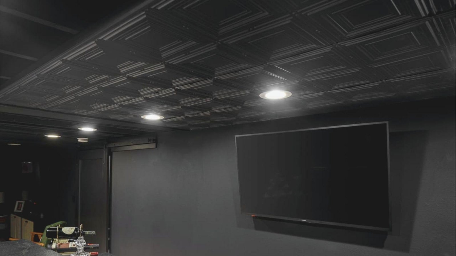 Modern basement media room featuring a black textured drop ceiling with geometric tile pattern and recessed lights.