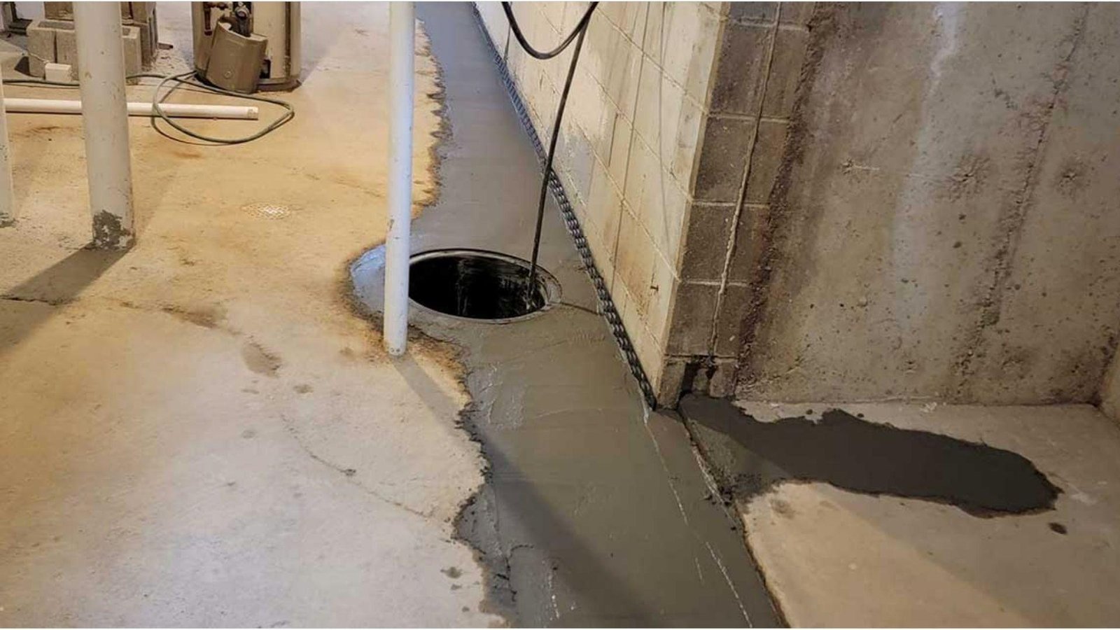 Completed interior French drain system with fresh concrete along basement wall and sump pump basin for basement waterproofing