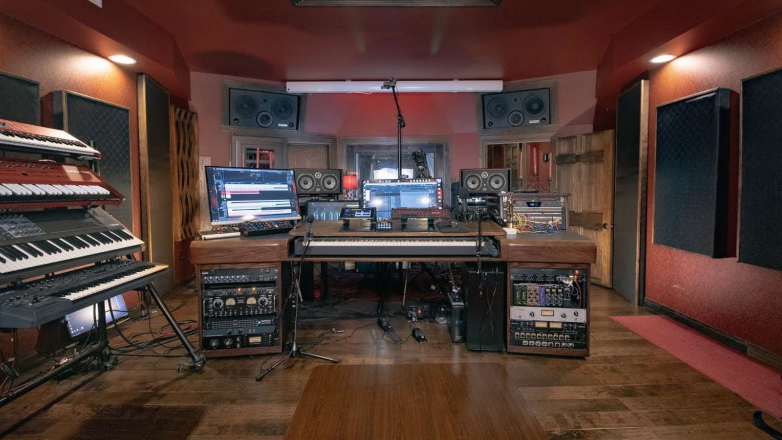 Pro basement recording studio with red walls, sound panels, keyboards, monitors and mixing desk.