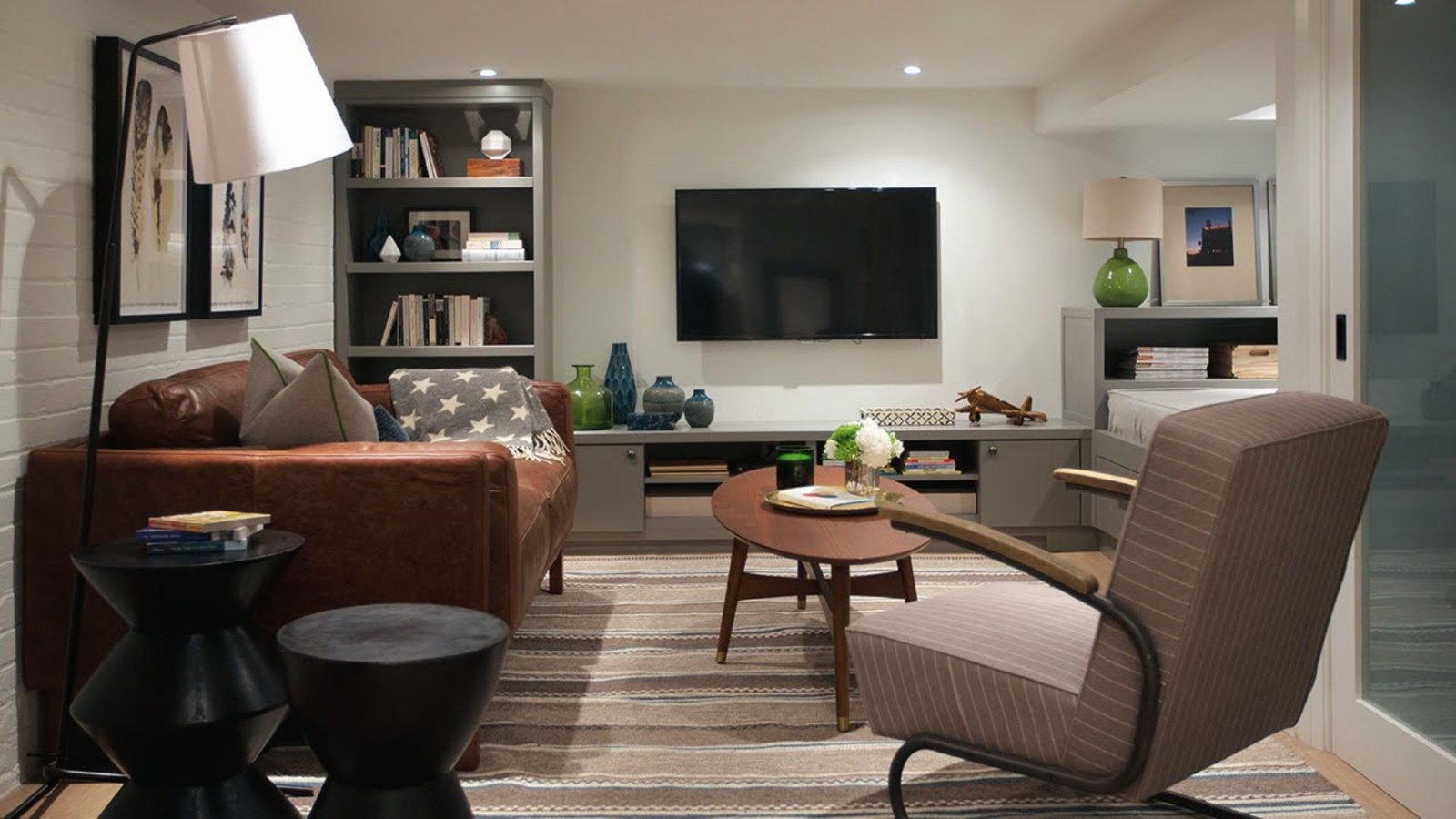 Industrial basement lounge with leather sofa, bookshelf wall, TV and mid-century modern furniture.