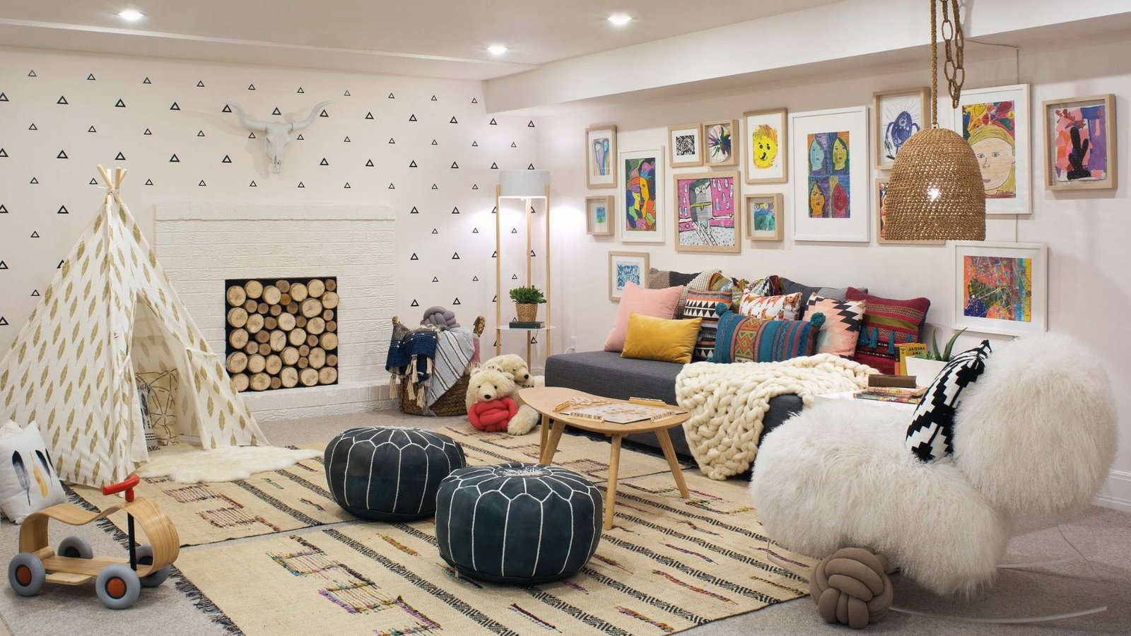 Playful basement kids lounge with teepee, poufs, art gallery wall, fireplace and colorful pillows.