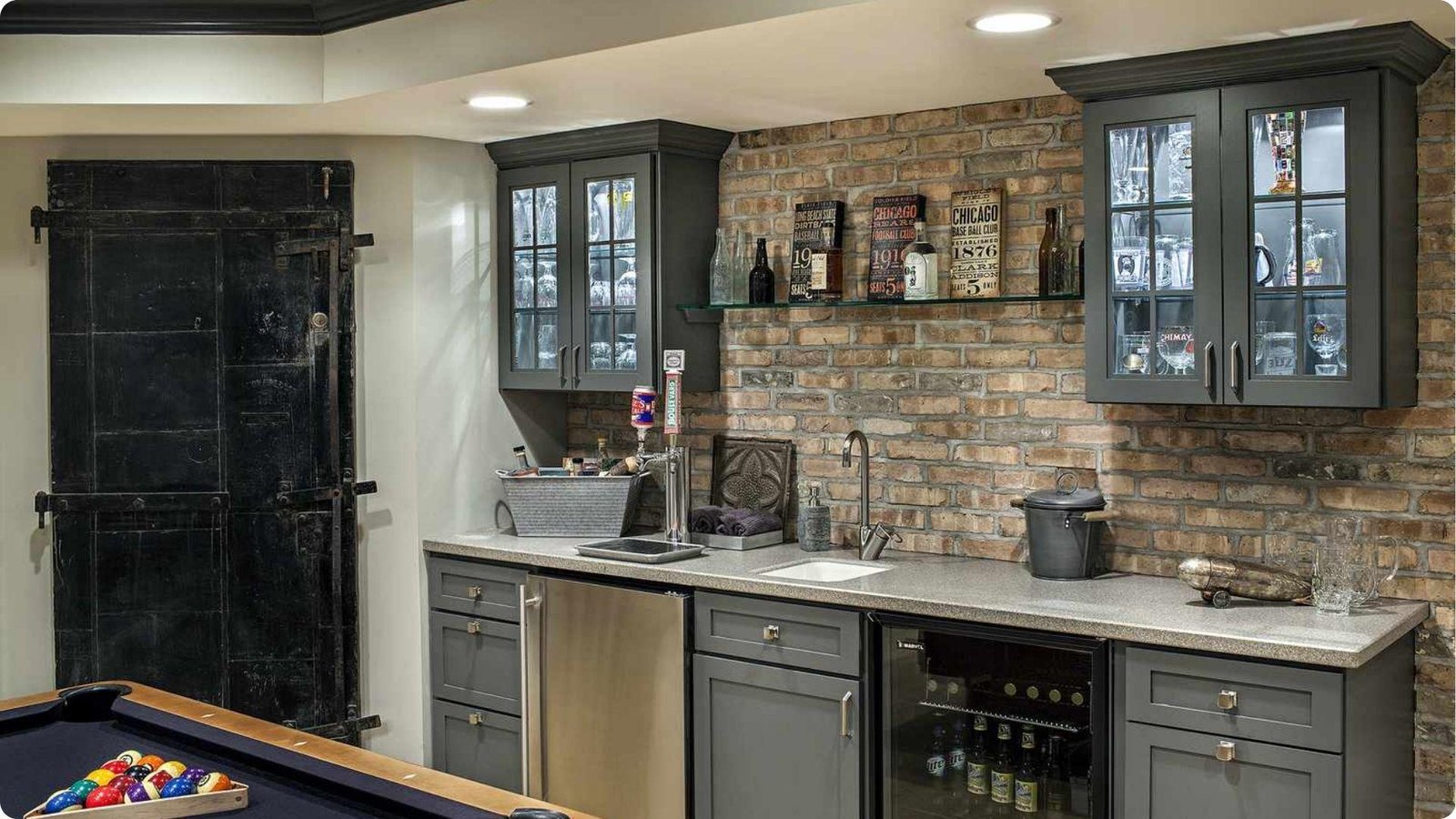Industrial-style basement kitchenette featuring exposed brick walls, gray cabinets, and glass-front uppers.