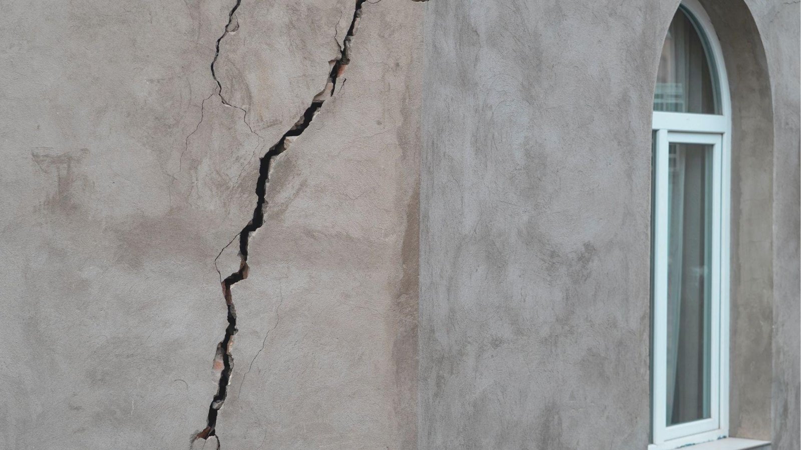 Large vertical crack splitting a gray concrete basement wall near an arched window.
