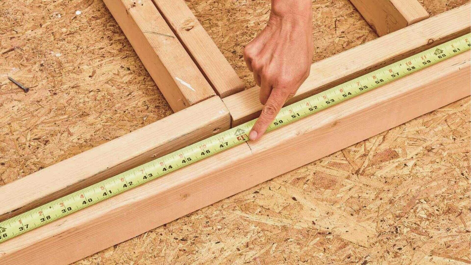 Close-up of a hand using a tape measure to mark a stud layout on a bottom plate for a floating basement wall.