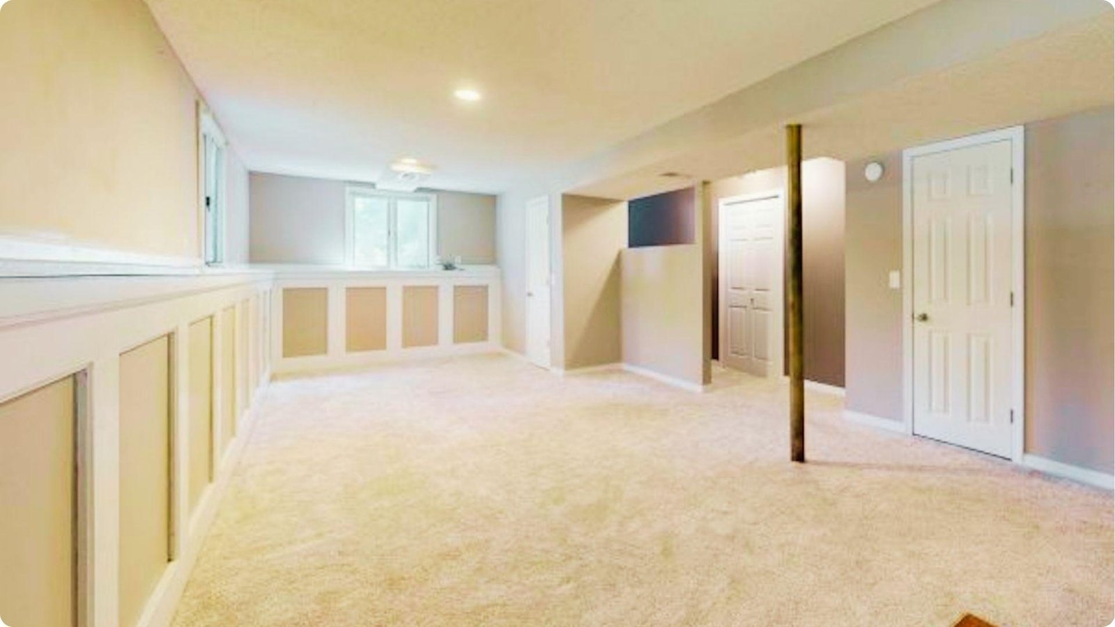 Finished basement featuring carpet flooring, painted walls with wainscoting, and a dropped ceiling with recessed lights.