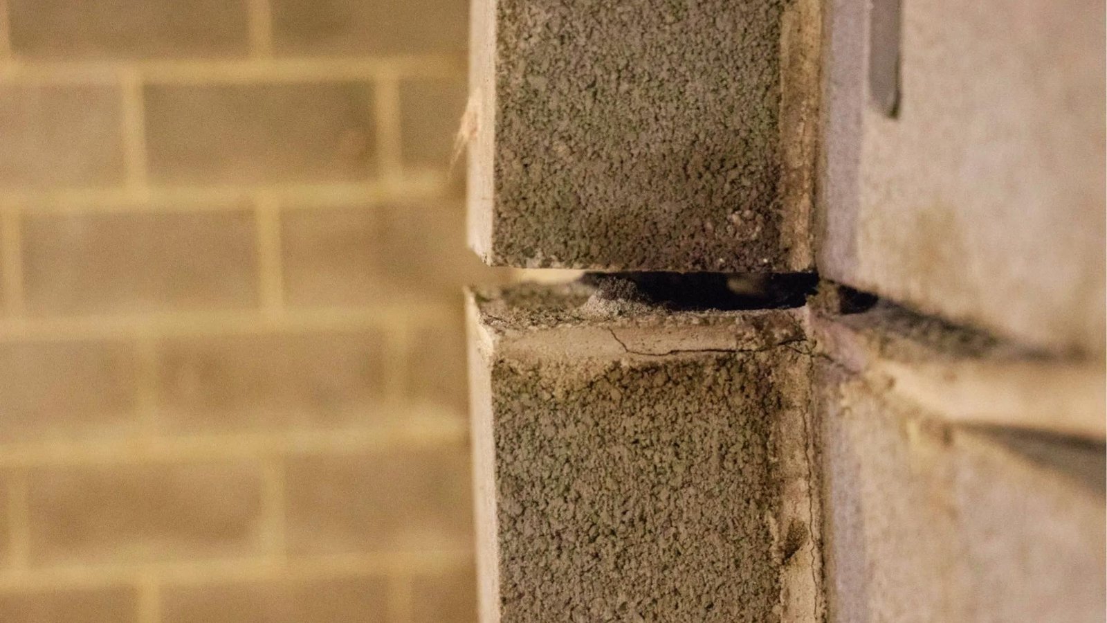 Close-up of concrete block wall with wide horizontal separation and crumbling mortar showing advanced structural failure and inward movement.