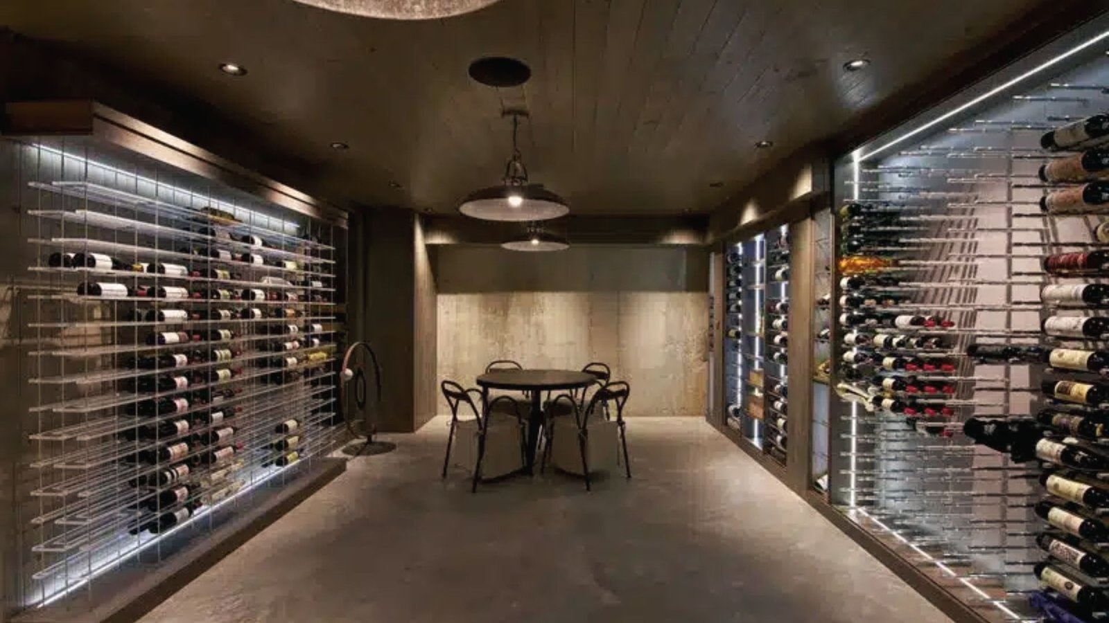 Rustic basement wine cellar with glass door, wood racks, stone arch, chandelier and lounge chairs.