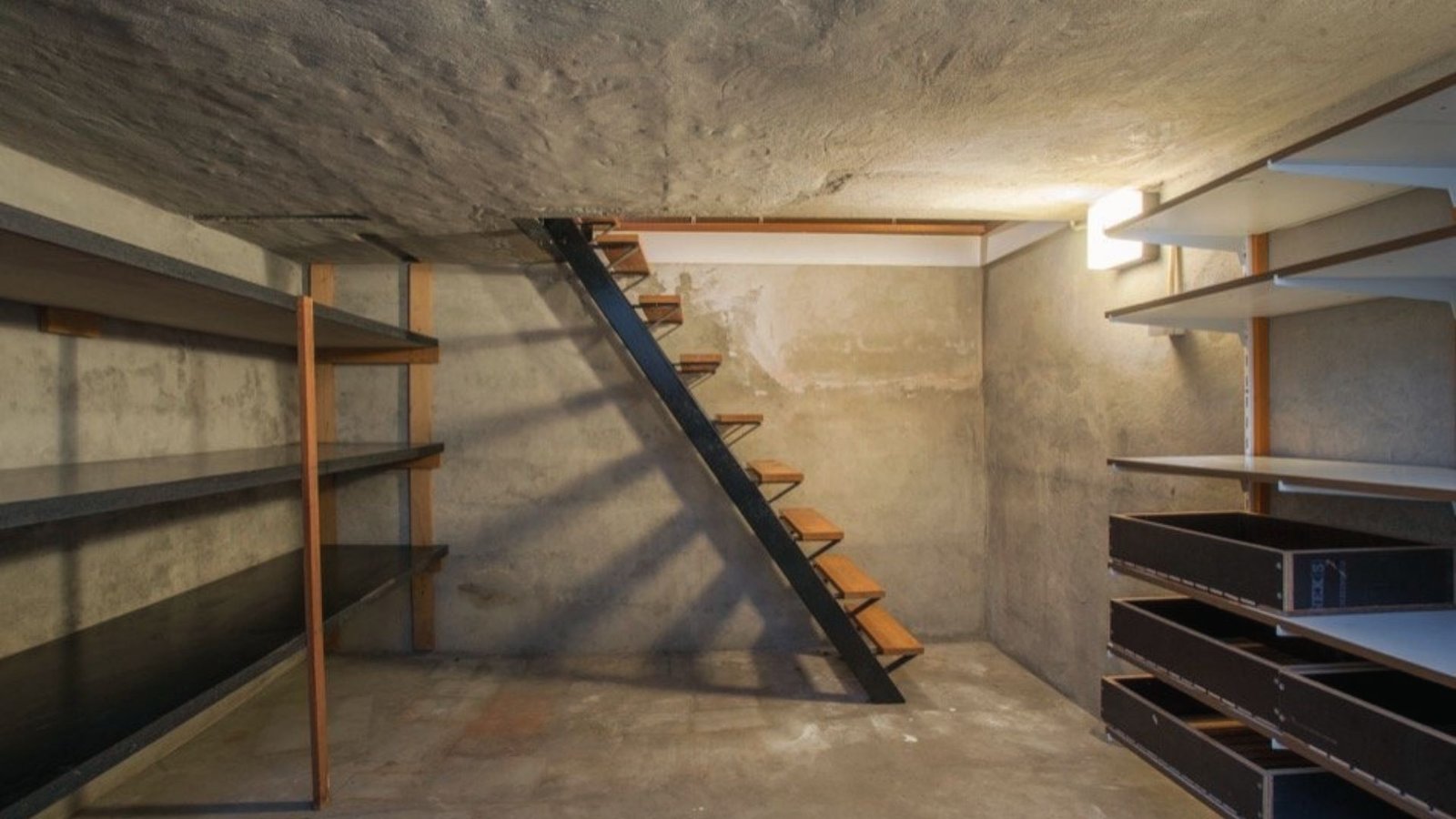 Unfinished basement with concrete walls, floor, and staircase for storage contrasting crawl space height.