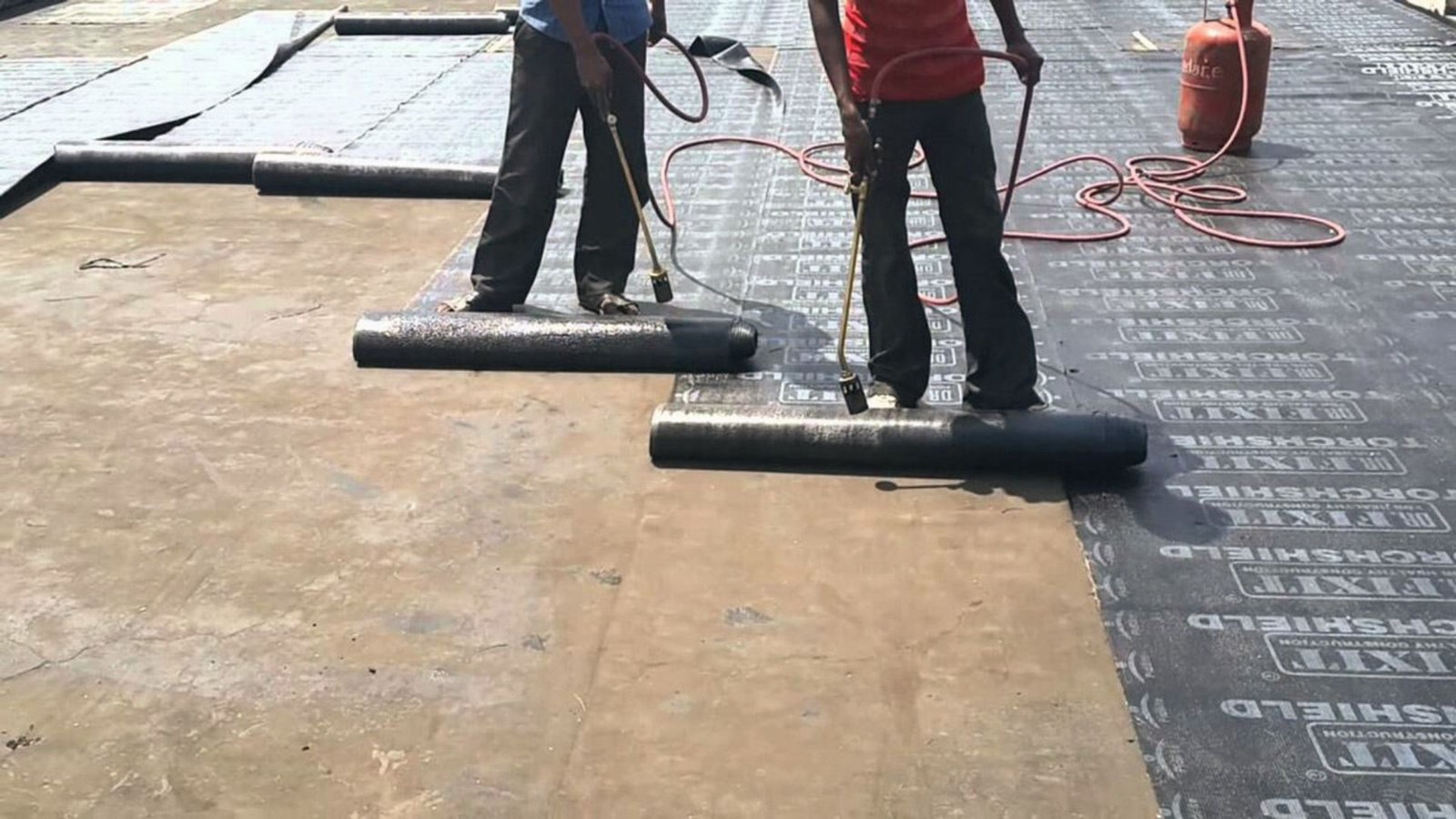 Contractors torch-applying waterproof membrane rolls on flat surface for heavy-duty basement sealing