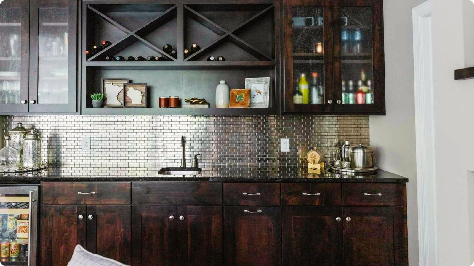 Traditional basement wet bar with dark wood cabinetry, metallic tile backsplash, and wine rack storage.