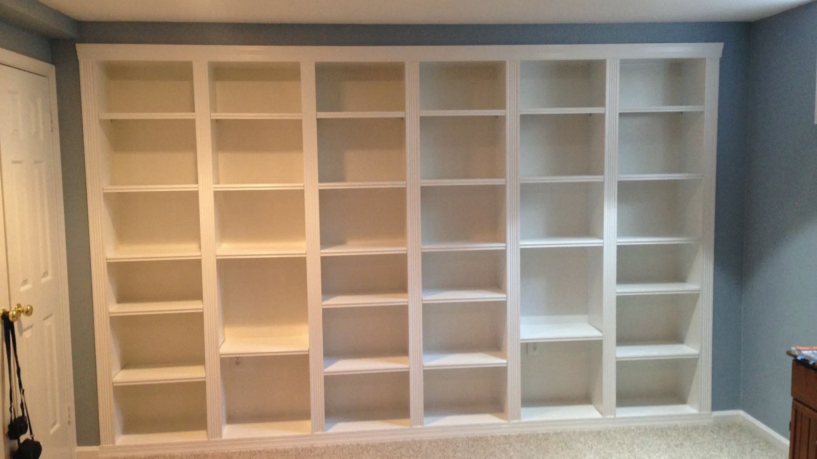 Basement library nook with floor to ceiling white built-ins, blue walls and carpet for reading.