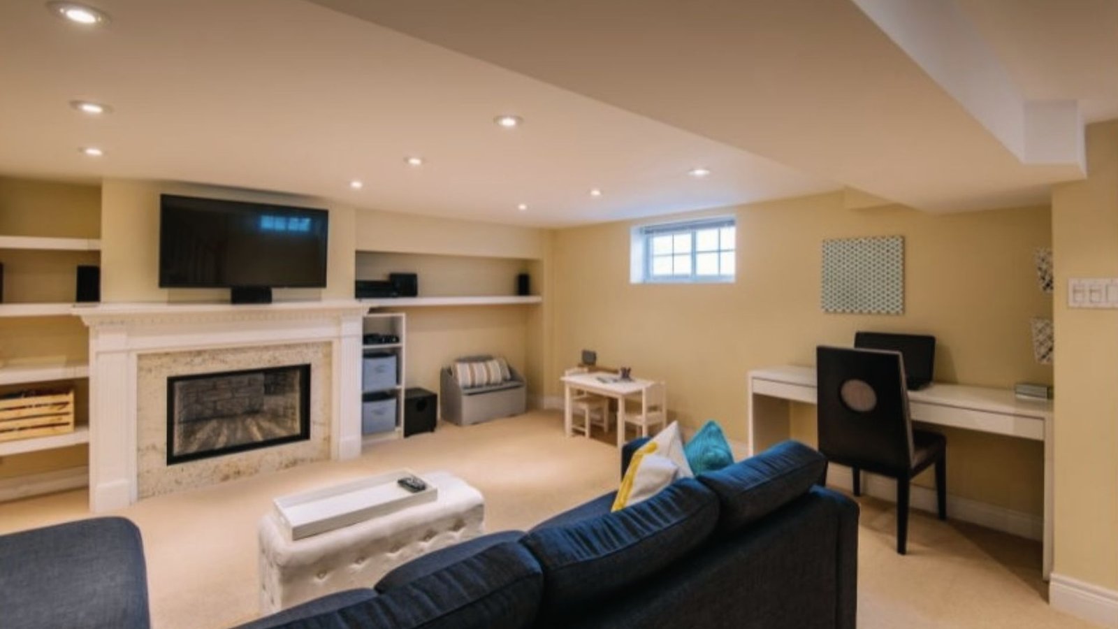 Cozy basement media room with fireplace, wall TV, blue sofa, desk nook and kids table for play.