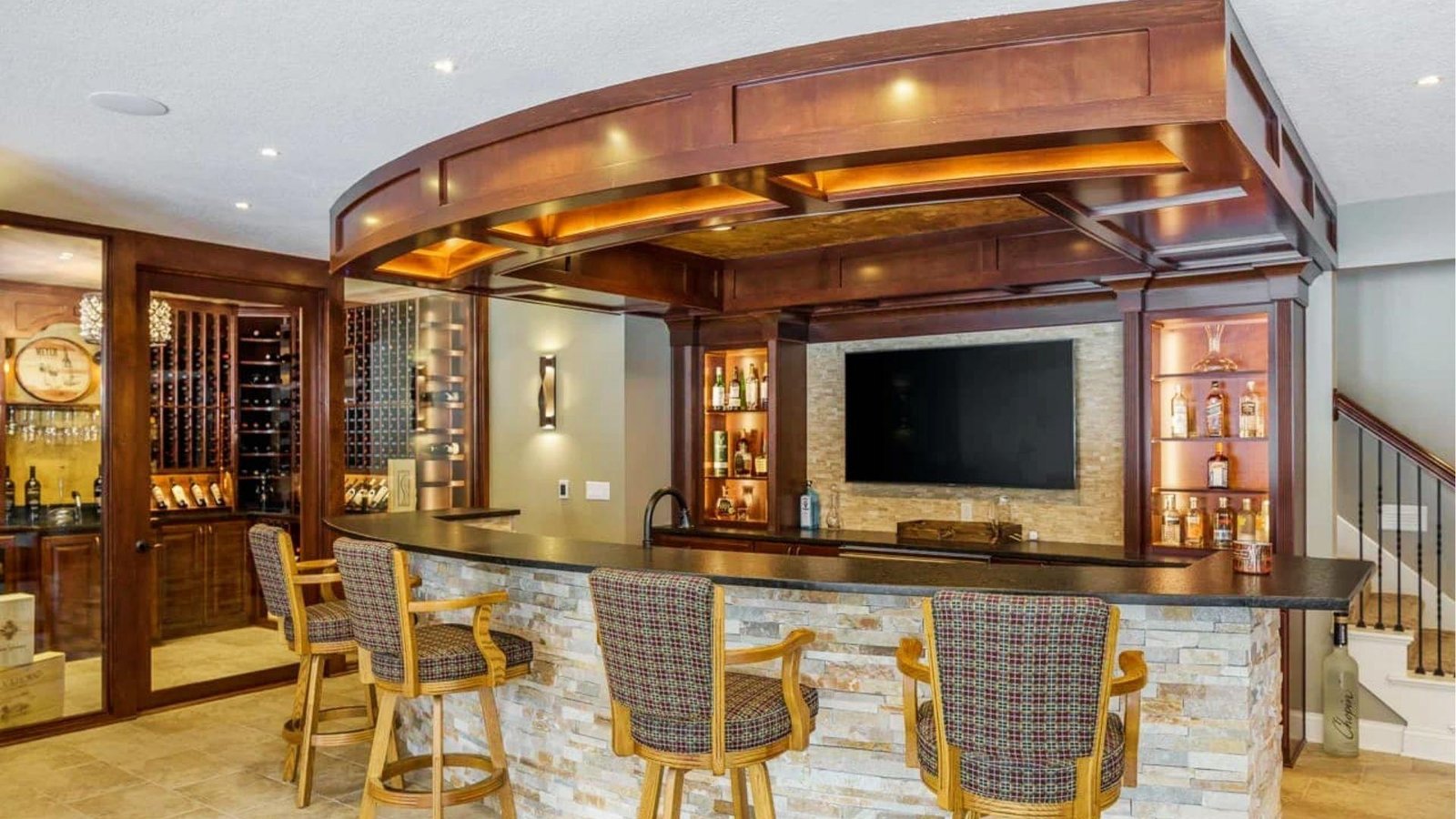 Luxury finished basement bar with wood cabinets, stone counter, wine cellar, and TV showing high-end basement finishing cost options.