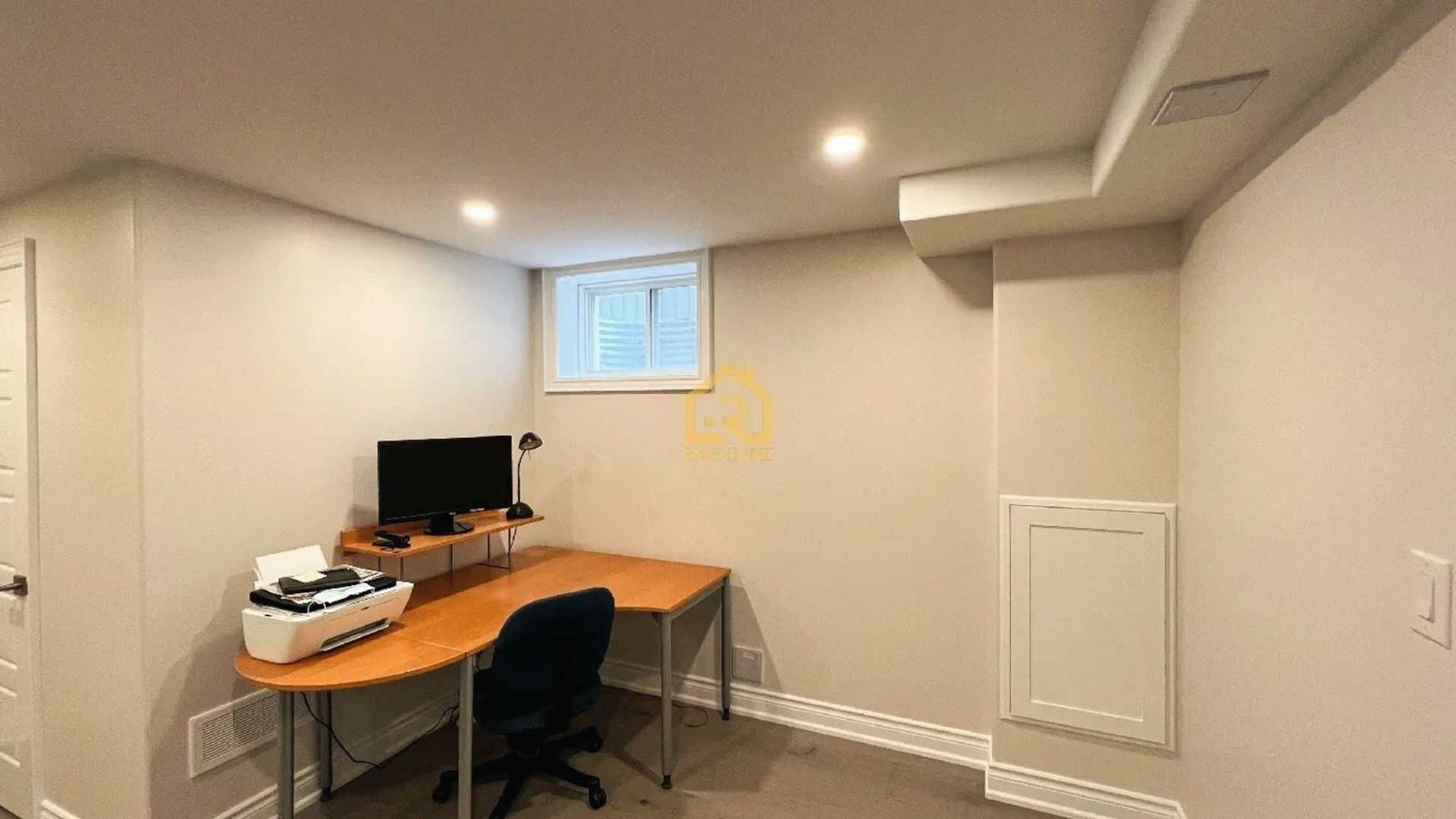Minimal basement workspace with corner L-desk, monitor, printer and egress window for home office.