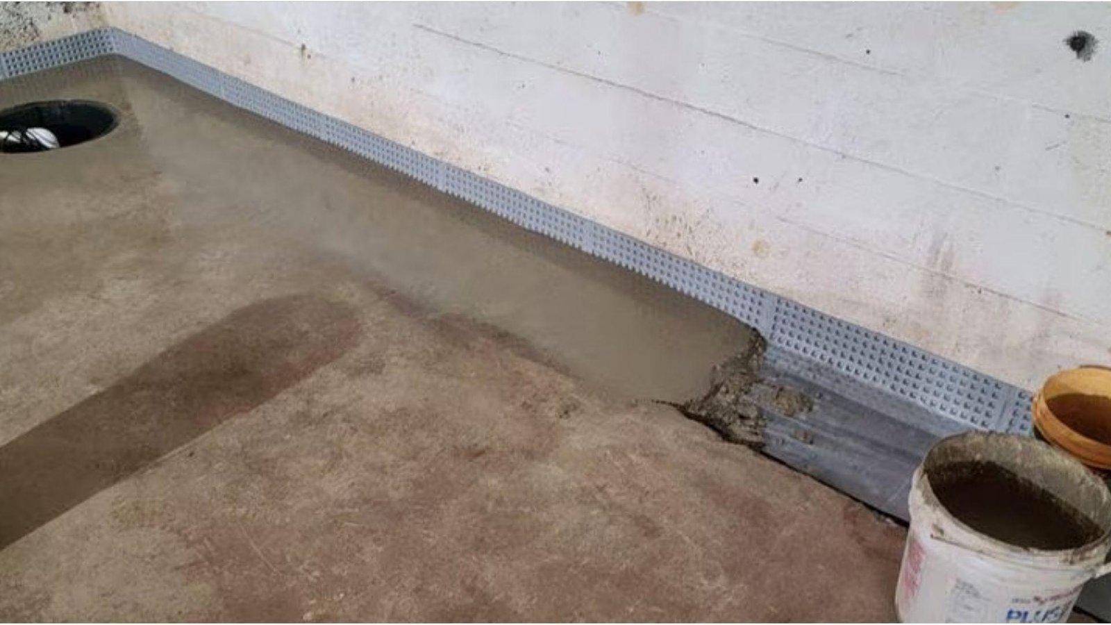 New interior French drain system installed along basement wall with fresh concrete and sump pump for waterproofing