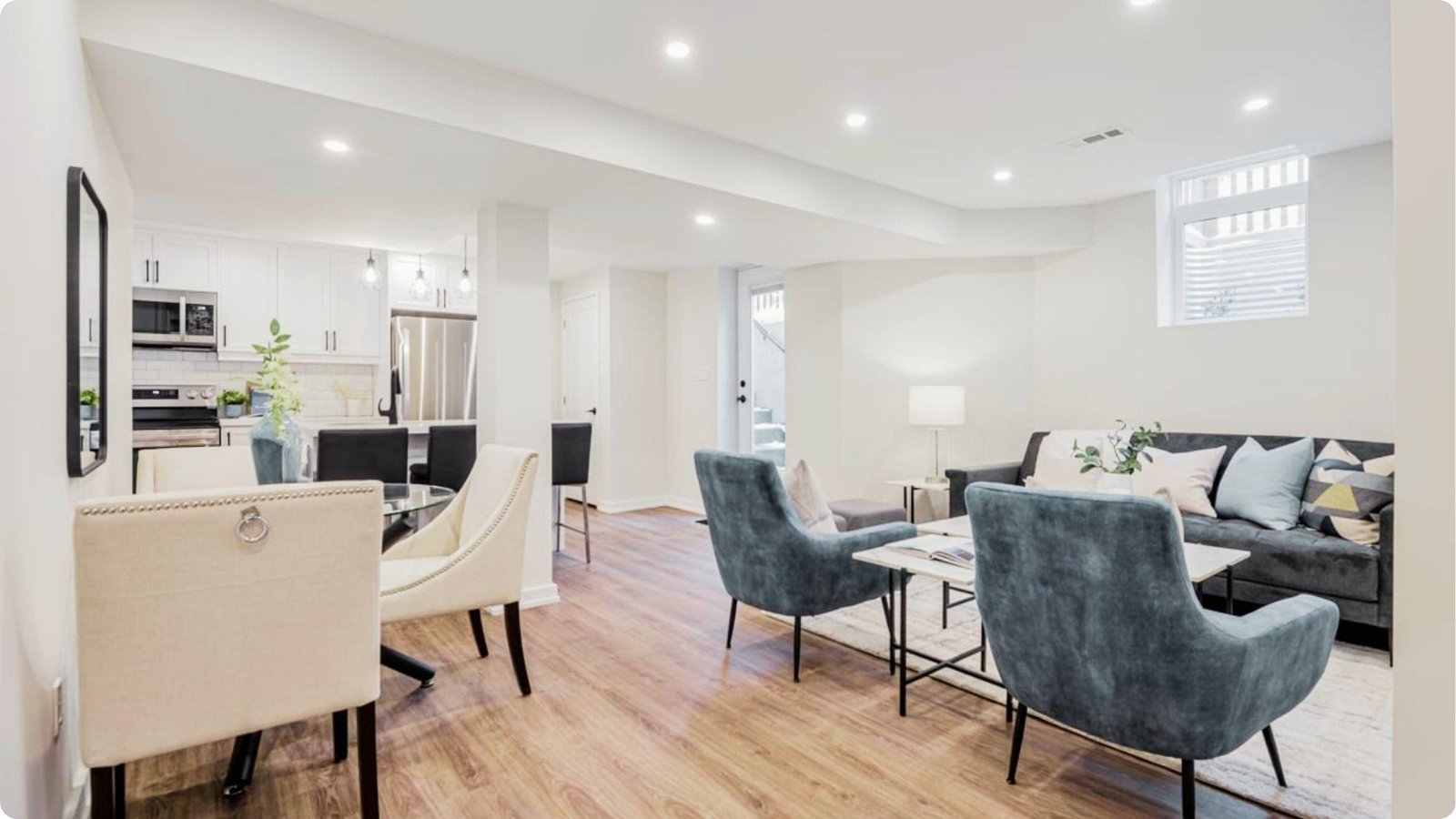 Bright open-plan English basement with white walls, wood flooring, and a glass dining set next to a modern living area.