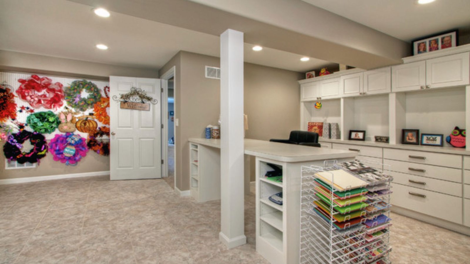 Basement craft room with white built-ins, paper rack, pegboard wreath wall and large work table.