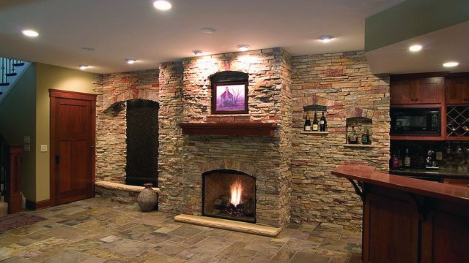Rustic stone fireplace in basement bar area with wood mantel, wine racks and stone tile flooring.