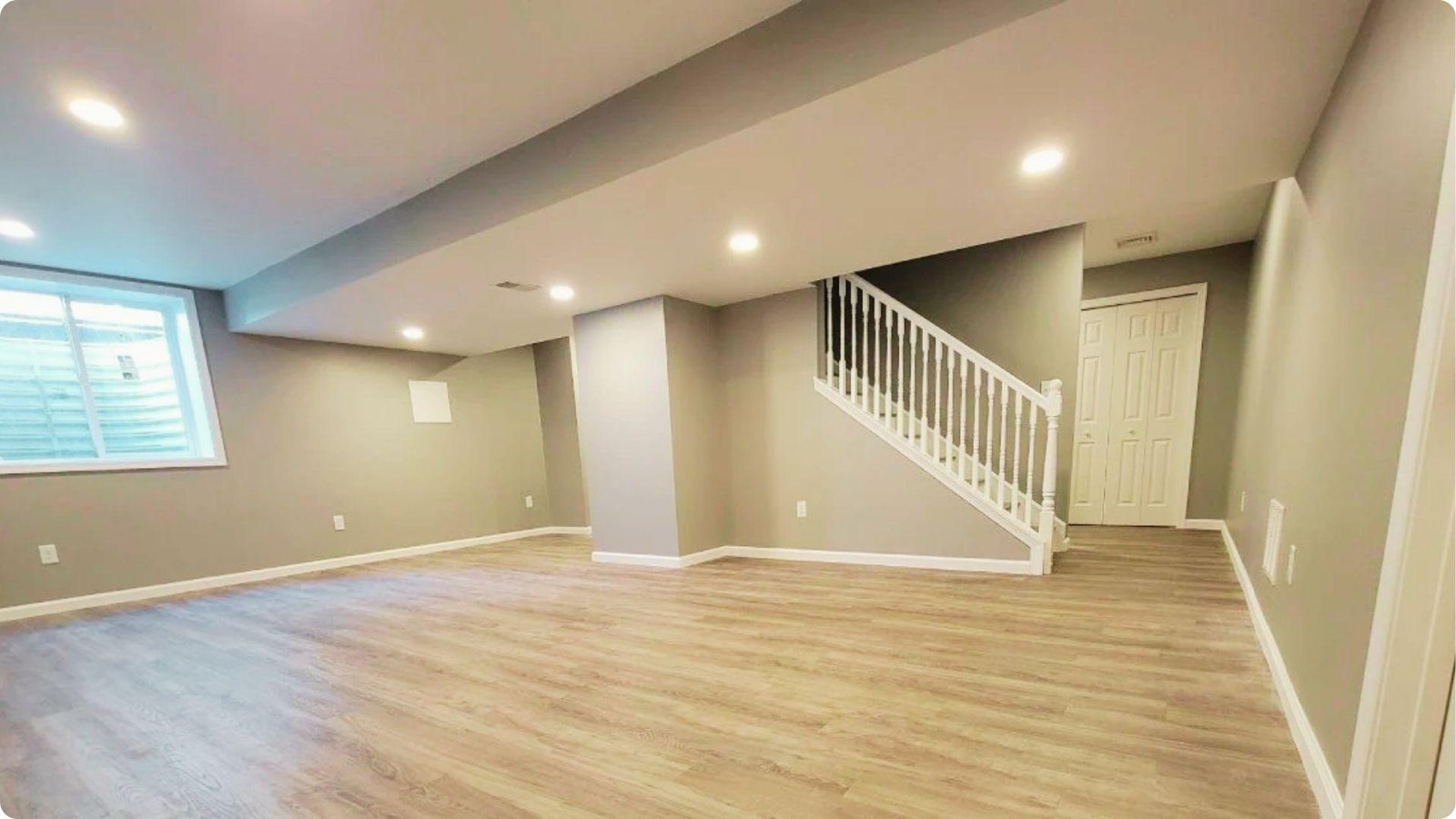 Finished basement with light wood-look flooring, recessed lighting, and painted drywall.