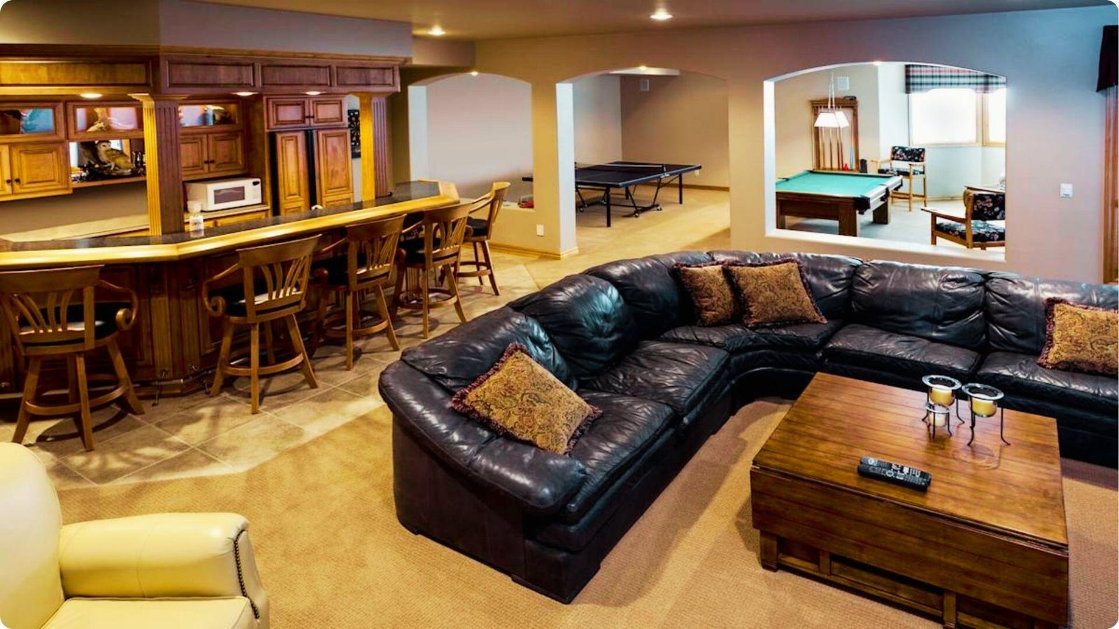 Spacious English basement rec room featuring a wet bar with wood cabinetry, large leather sectional, and carpeted floors.