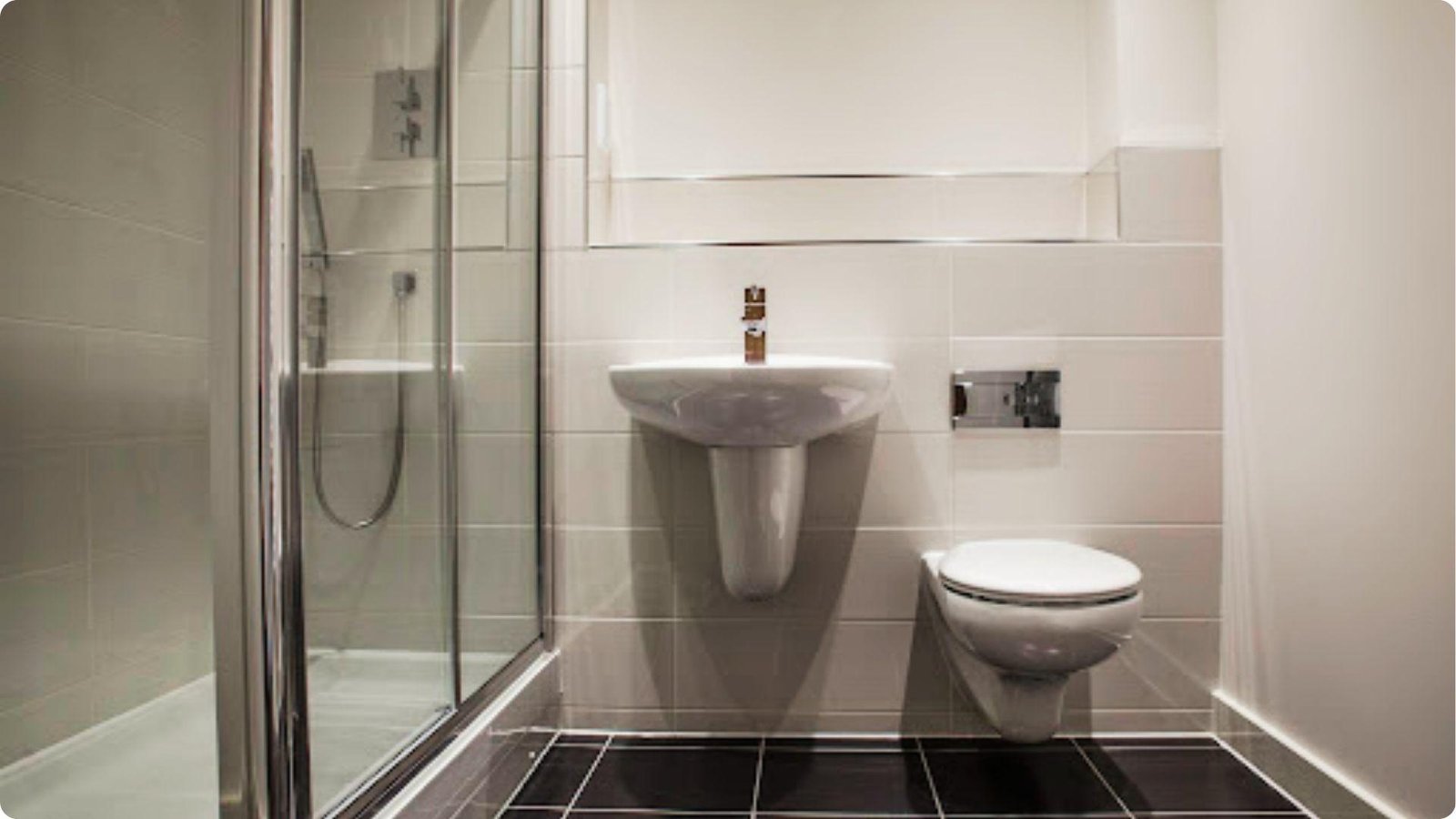 Compact basement bathroom with wall-mounted toilet, pedestal sink, and glass shower stall.