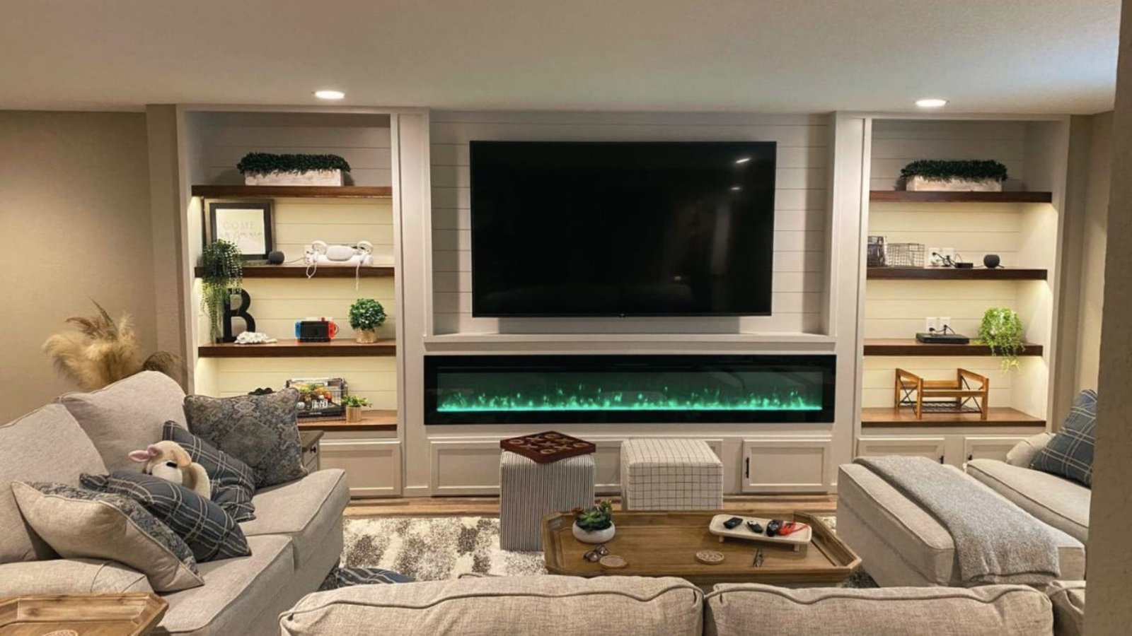 Cozy basement media room with TV wall, electric fireplace, built-ins and gray sectional sofas.