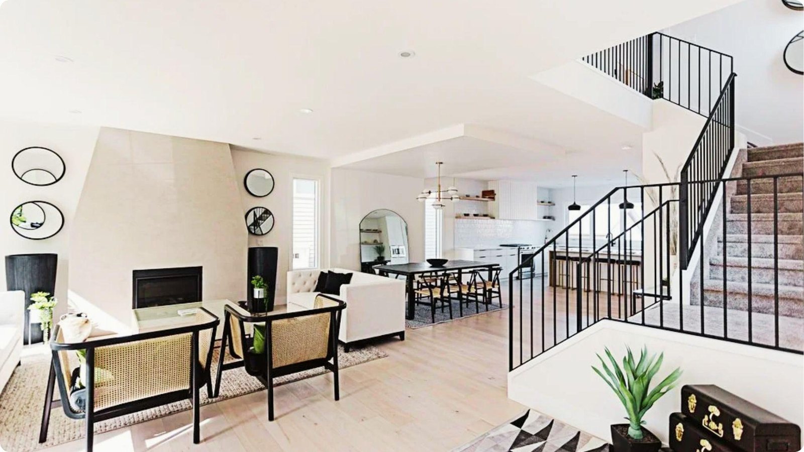 Open-plan English basement with light wood floors, white walls, and a staircase with black railings.