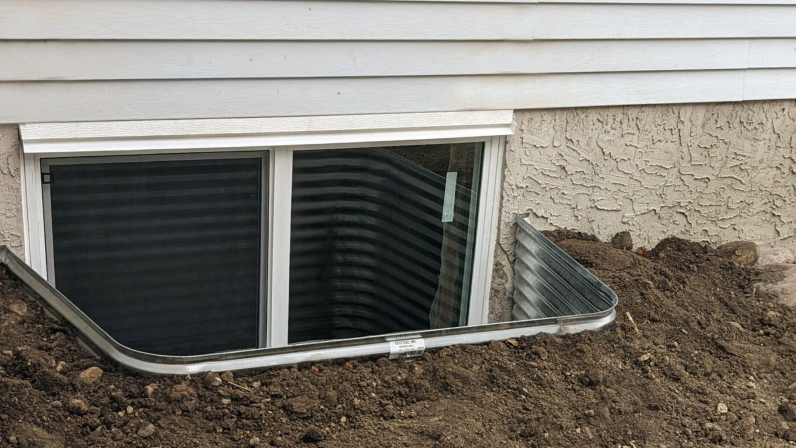 New basement egress window with metal well installed against siding for safety and natural light.