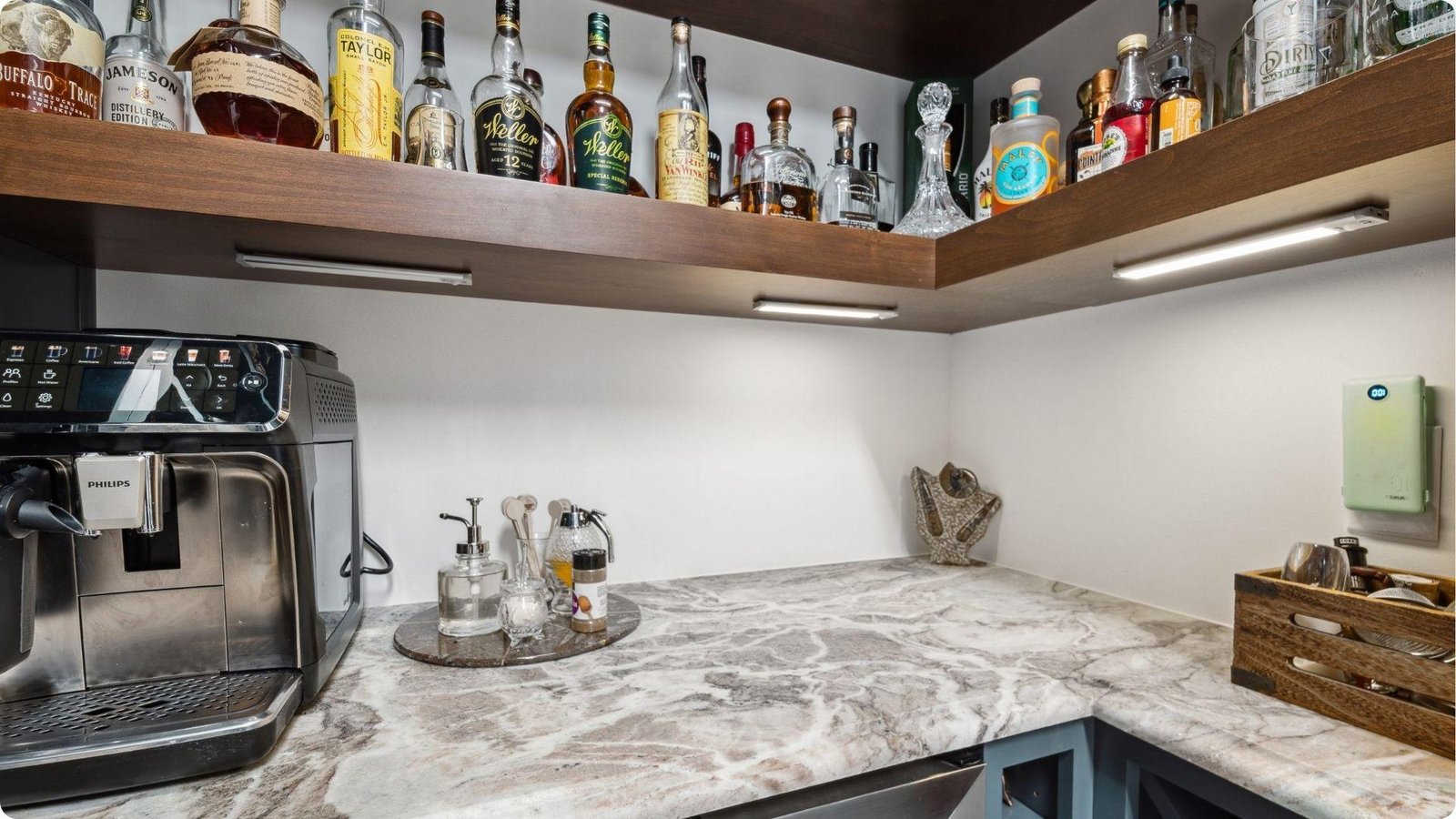 Compact basement coffee and cocktail bar with marble countertops and floating wood shelves lined with liquor bottles.
