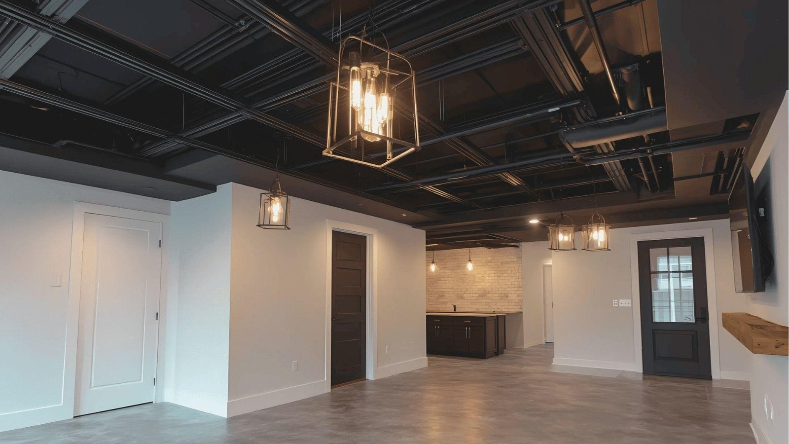 Spacious basement with an exposed black grid ceiling system and industrial pendant lighting over polished concrete floors.