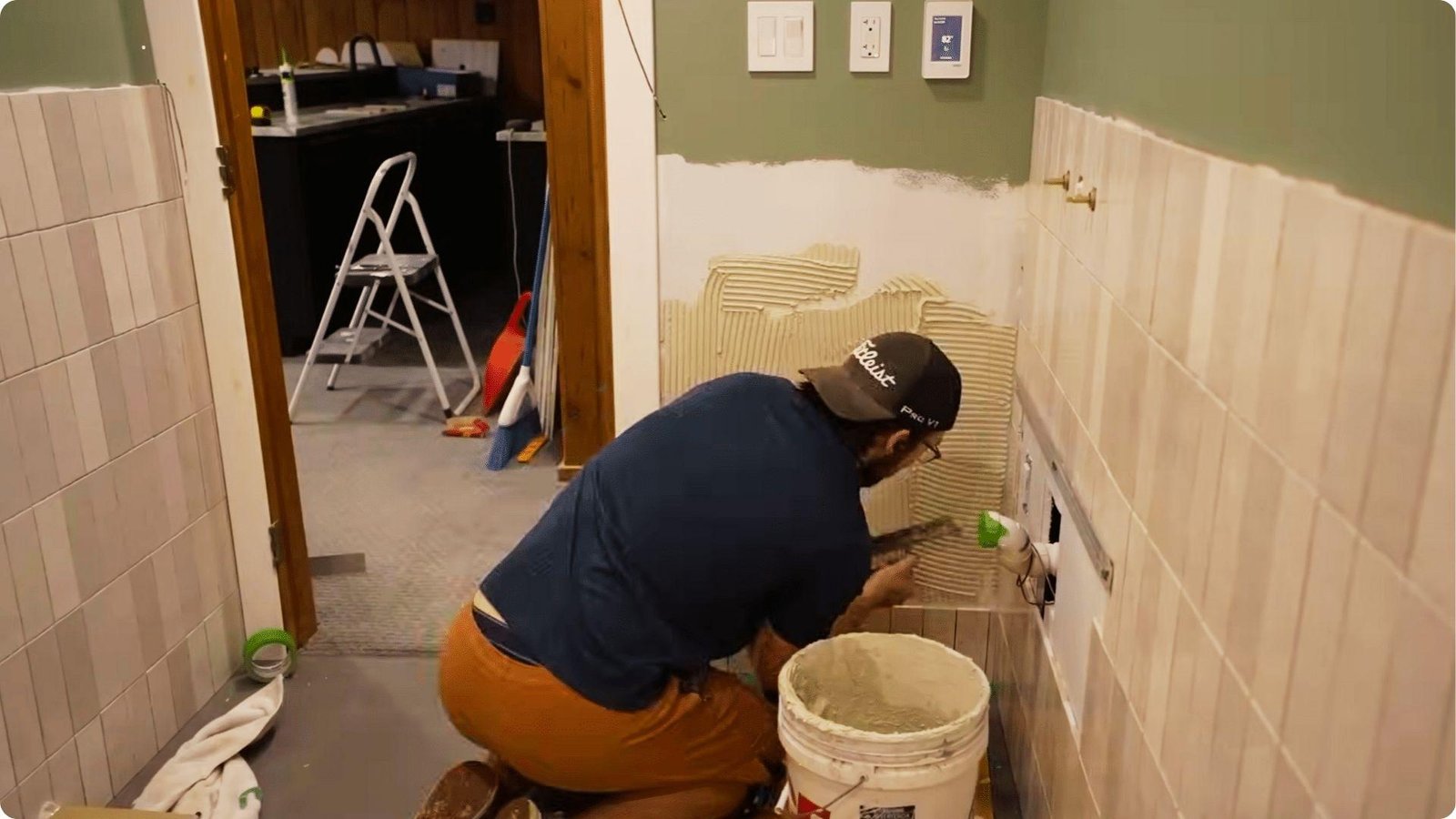 Man in cap spreading tile adhesive on unfinished basement bathroom wall during remodel.