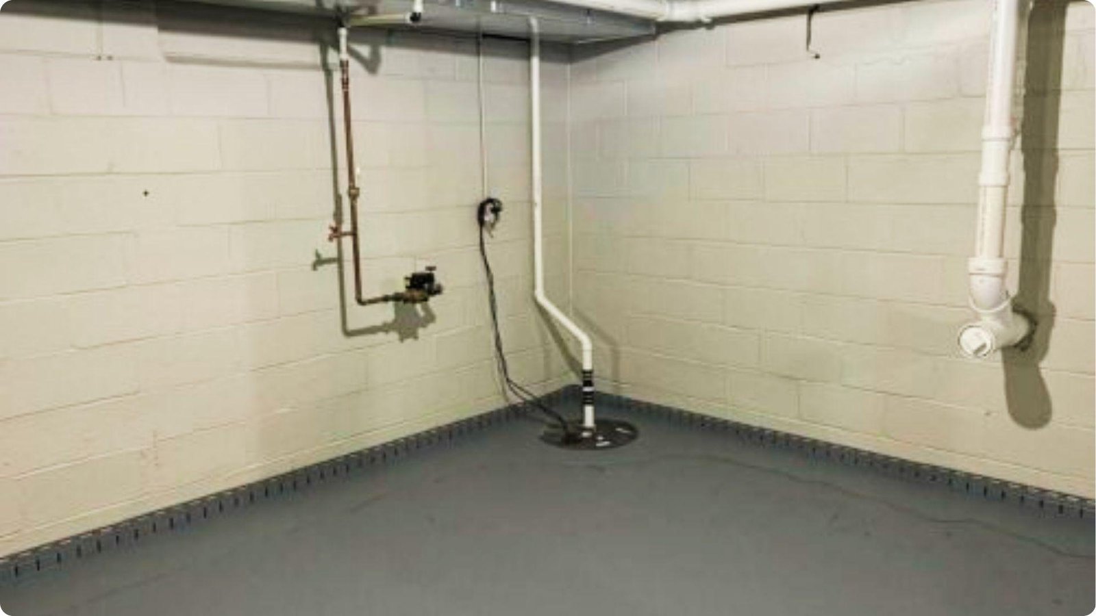 Basement corner with cinder block walls, sump pump, and a perimeter drain system installed along the floor joint.