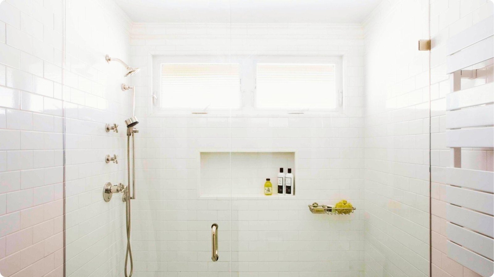 Bright white basement shower with subway tile, glass door, and built-in niche storage.