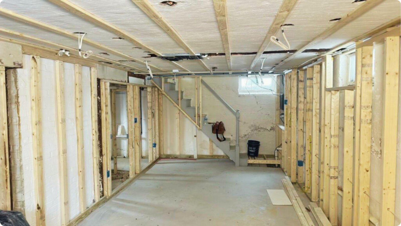 Basement framing in progress with rigid foam board insulation installed between wood studs on walls and ceiling.